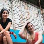 two women sitting on a wall with a brick wall behind them